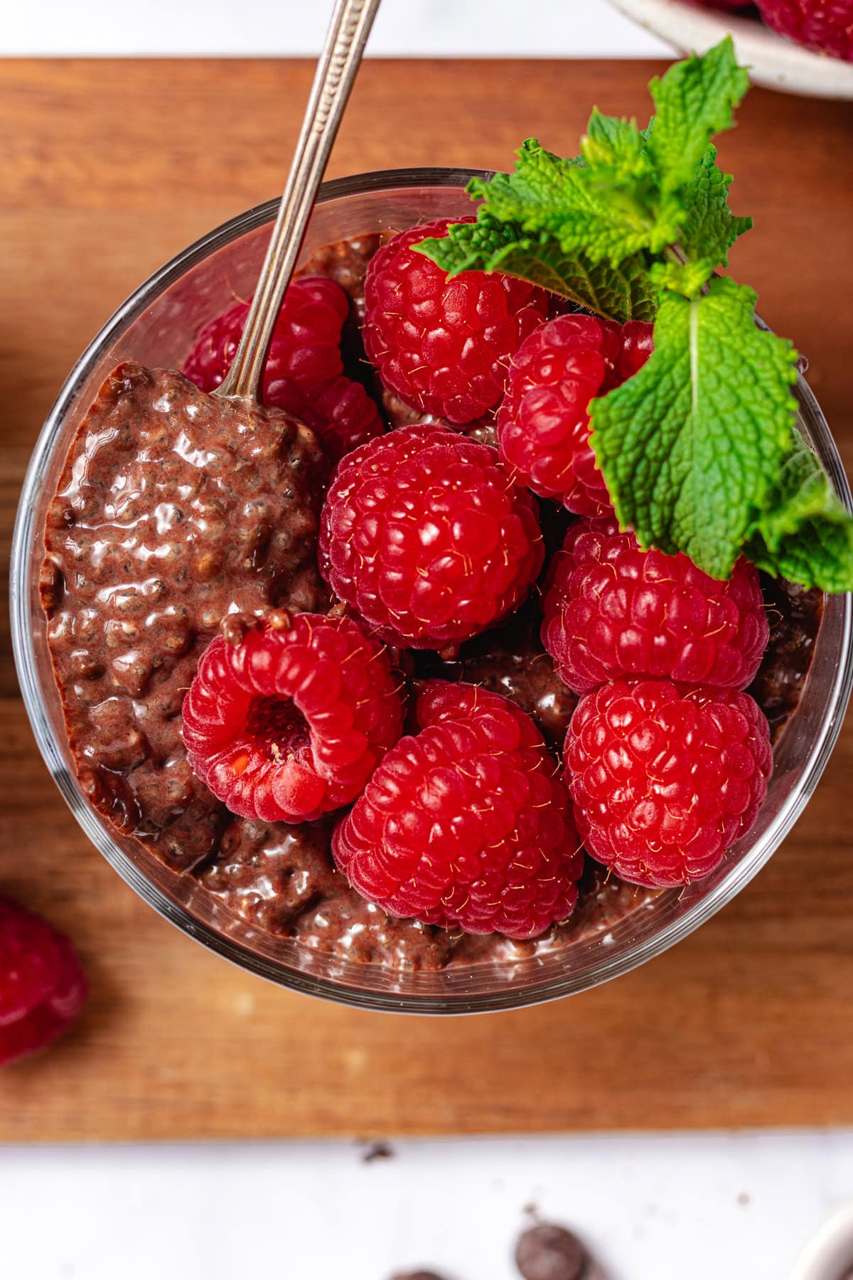 close up of chocolate chia pudding in jar with fresh raspberries and mint. 