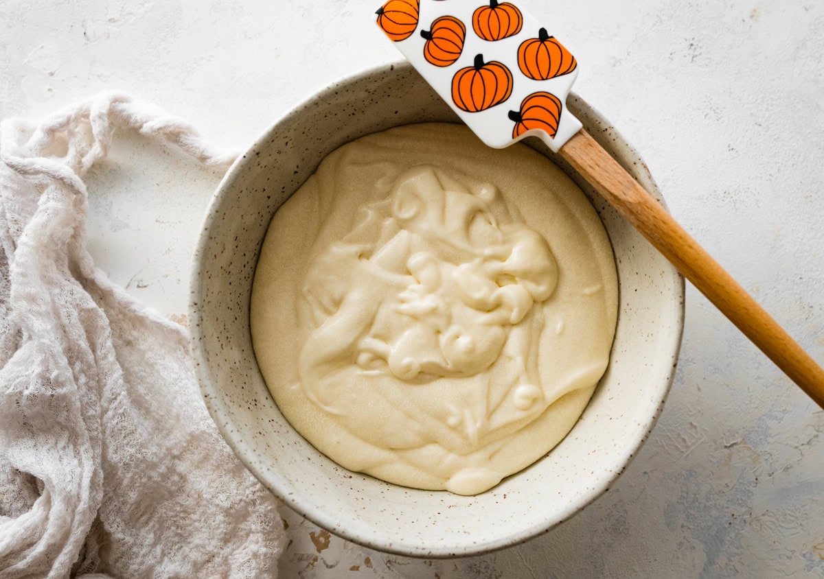 cream cheese icing in bowl with pumpkin spatula. 