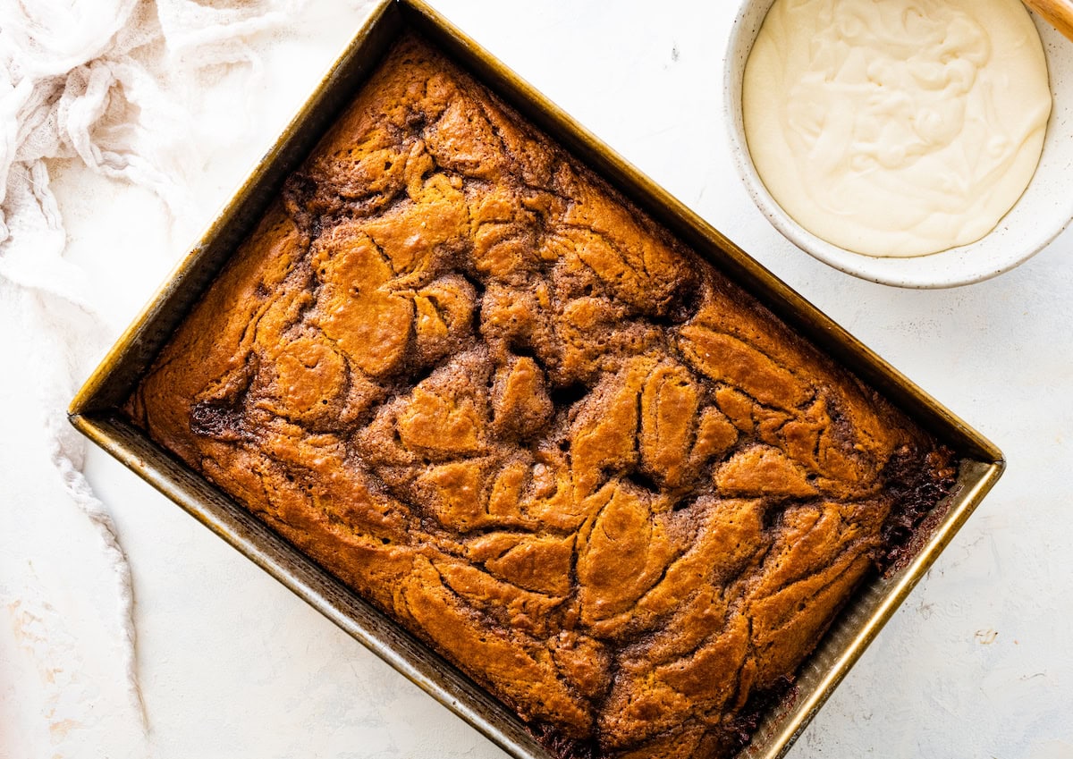 cinnamon swirl pumpkin cake in pan with bowl of cream cheese icing. 