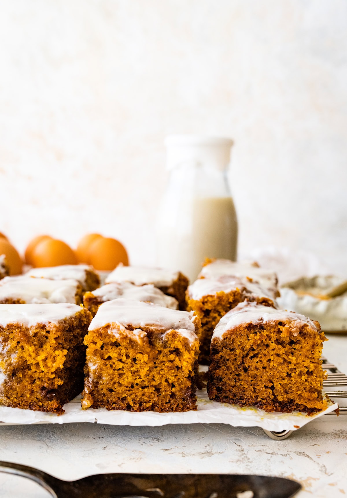 cinnamon swirl pumpkin cake cut into squares on cooling rack with bottle of milk. 