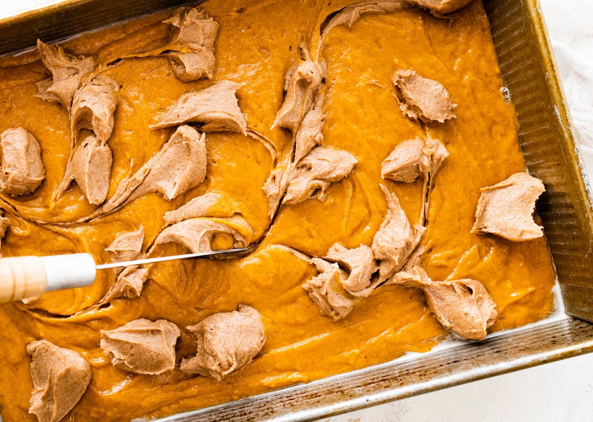 swirling cinnamon mixture into pumpkin cake batter with knife. 