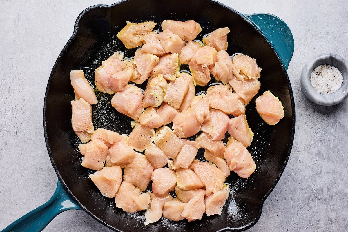 cut up chicken breasts cooking in cast iron skillet. 