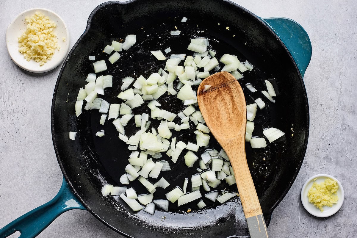 onion cooking in cast iron skillet with wooden spoon. 