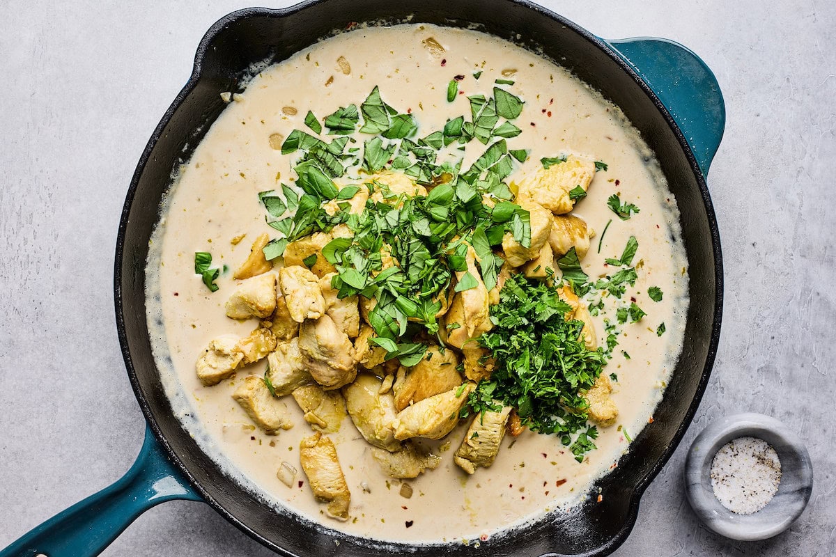 coconut lime chicken cooking in cast iron skillet with herbs. 