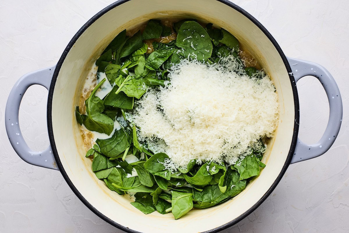 spinach and parmesan cheese being added to orzo in pot. 