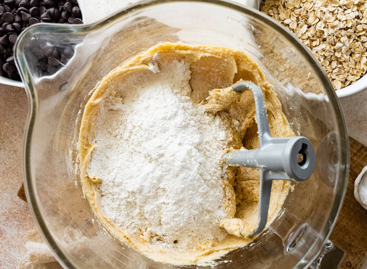 dry ingredients being added to wet ingredients in mixing bowl to make oatmeal chocolate chip cookies. 