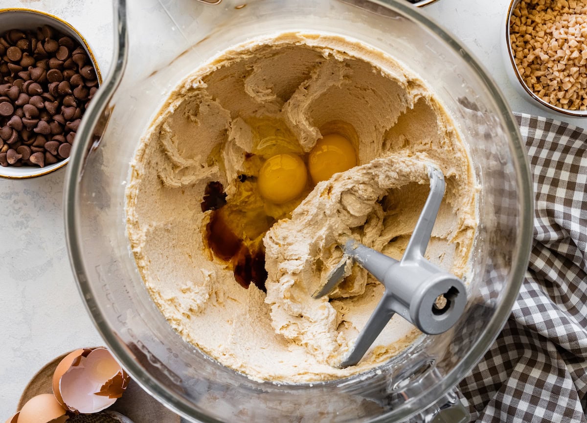 eggs and vanilla extract being added to creamed butter and sugars in mixing bowl. 