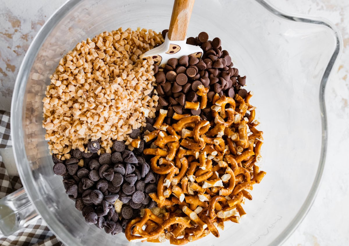 toffee, milk chocolate chips, pretzels, and semisweet chocolate chips being added to cookie dough. 