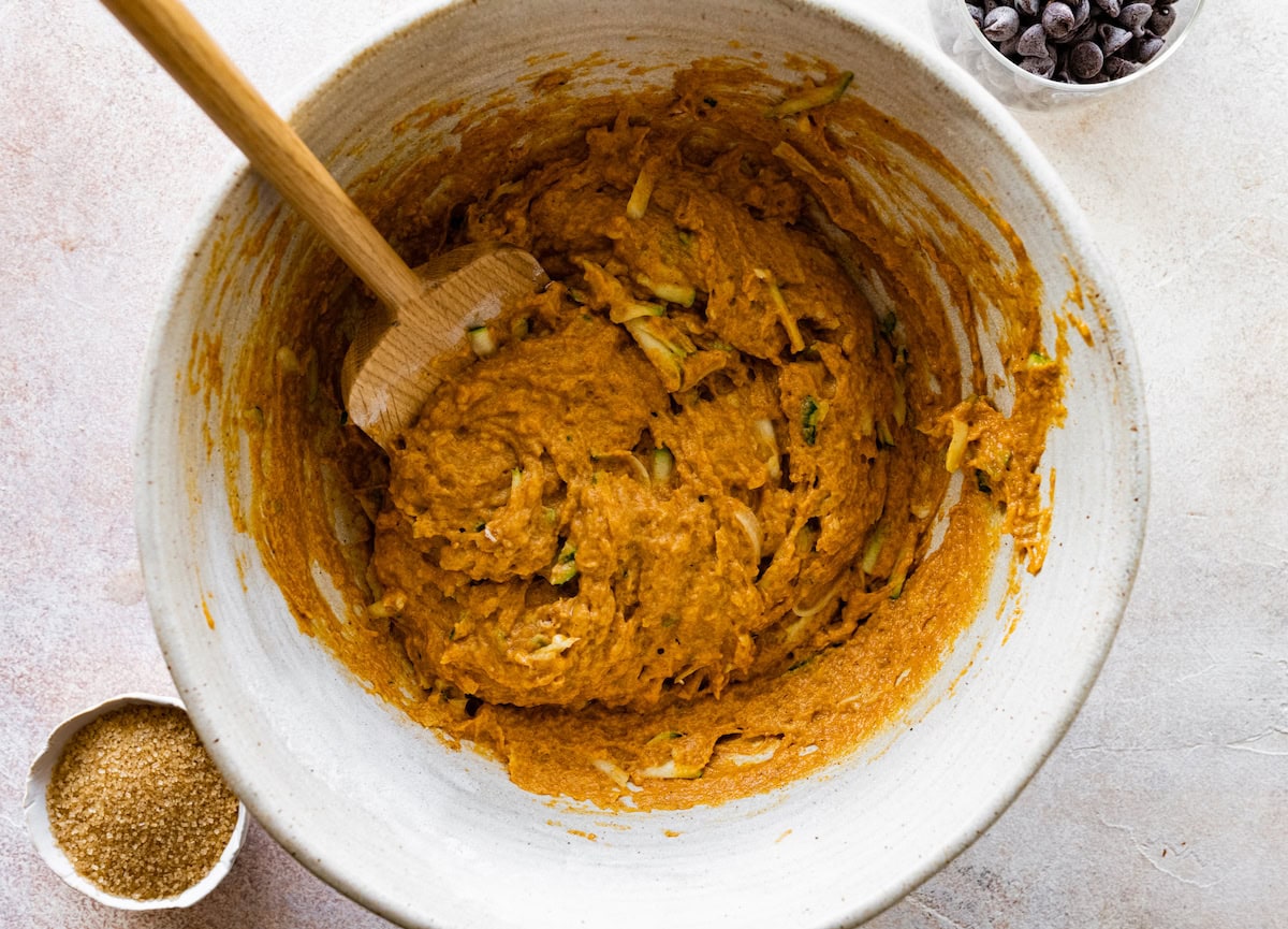 pumpkin zucchini batter in mixing bowl with wooden spoon. 