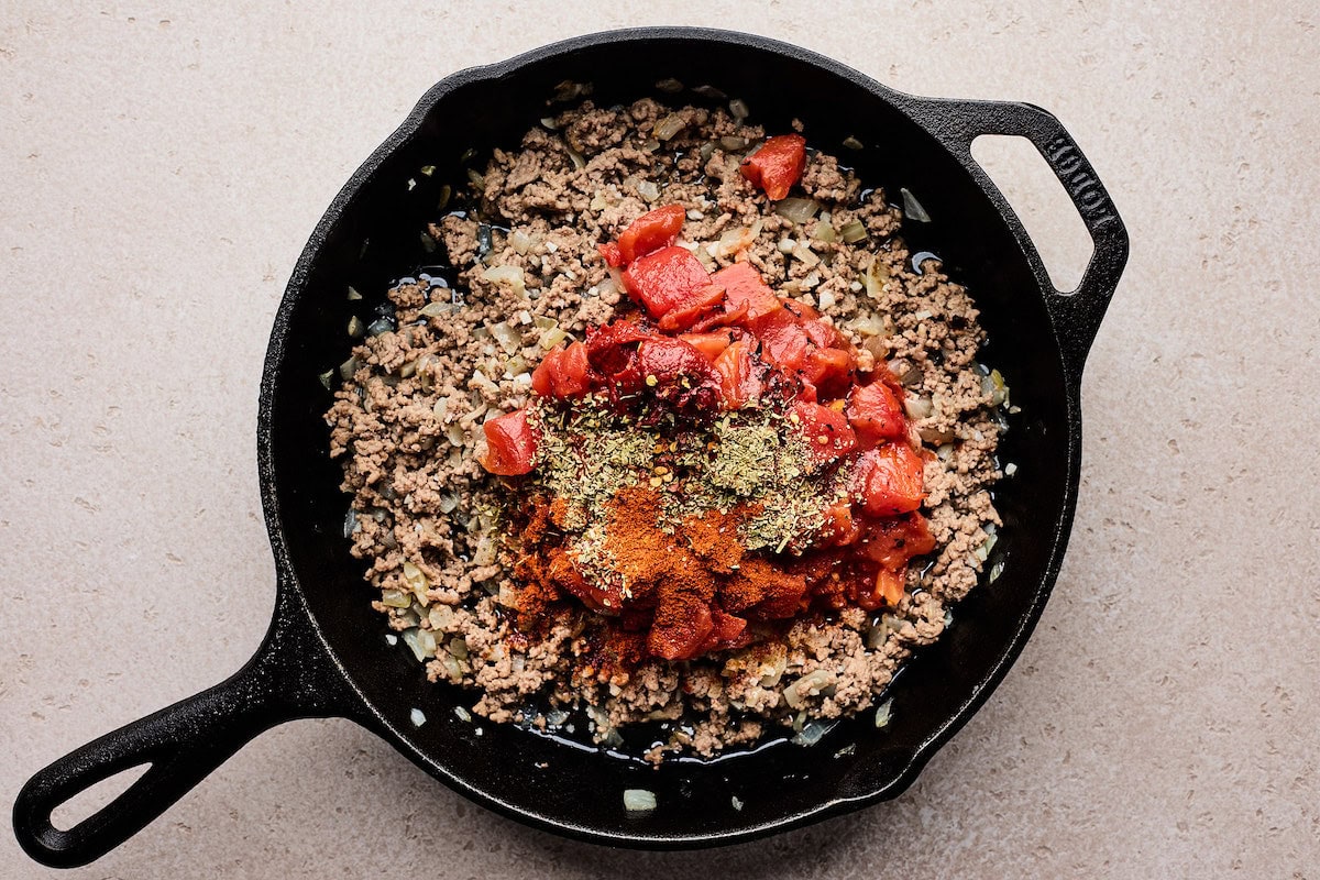 ground beef cooking in pan with onions, tomatoes, spices, and herbs to make stuffed peppers. 