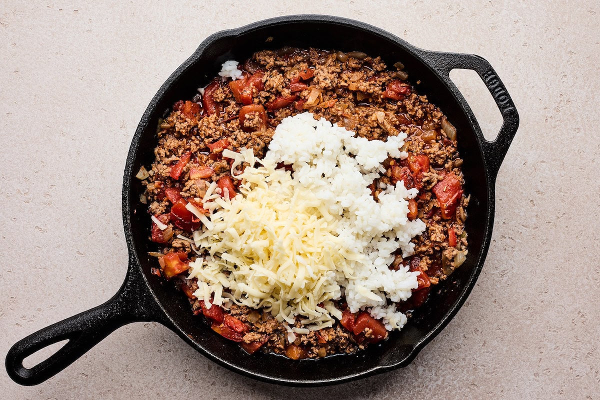 shredded cheese and rice being stirred into ground beef mixture to make stuffed peppers. 