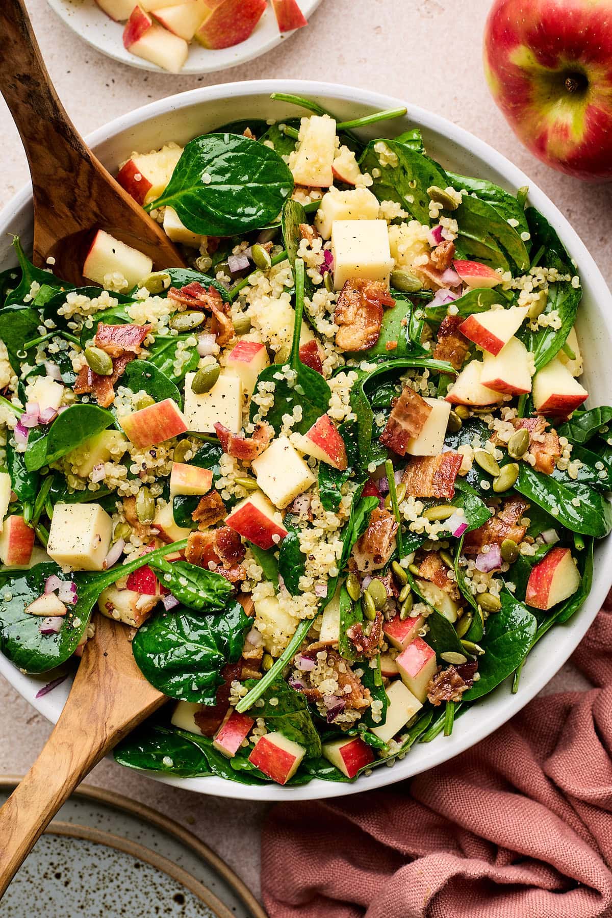 Apple, Bacon & White Cheddar Quinoa Spinach Salad in bowl with wooden salad servers. 