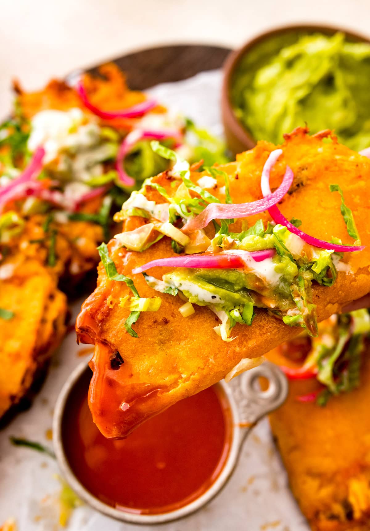 crispy buffalo chicken taco being dunked in buffalo sauce. 