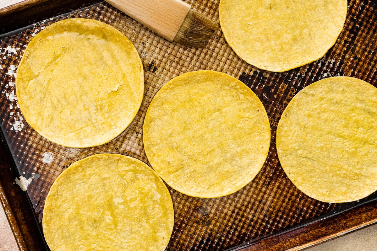 corn tortillas being brushed with oil on baking sheet to make crispy buffalo chicken tacos. 