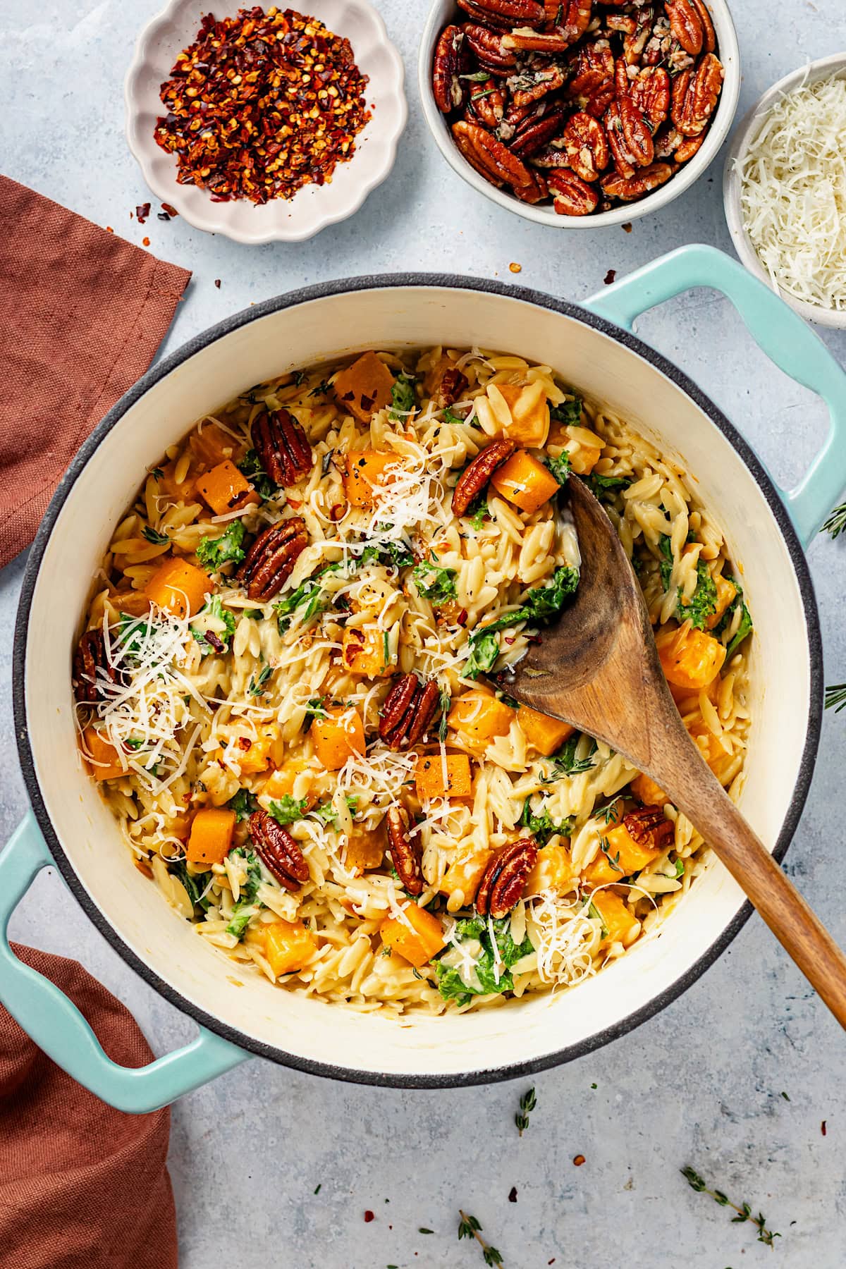 butternut squash orzo in pot with pecans, parmesan cheese, and wooden spoon. 