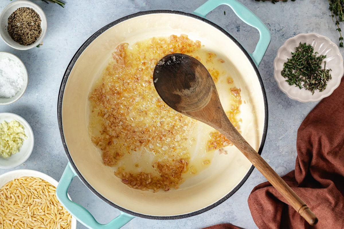 shallot and garlic cooking in pot with wooden spoon. 