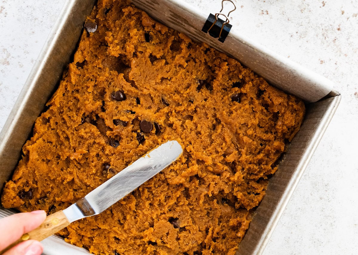 flourless peanut butter blondie dough being spread in pan lined with parchment paper. 