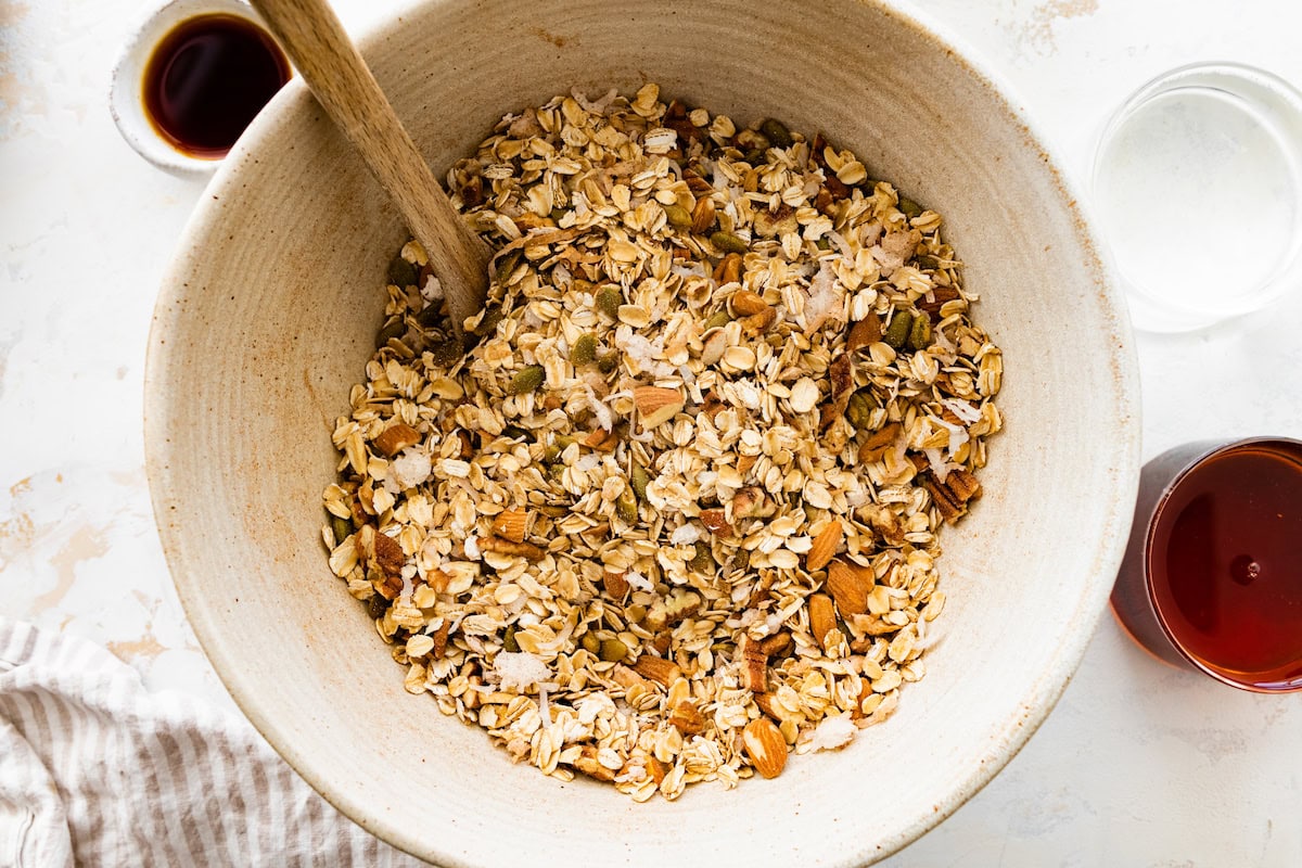 granola ingredients in mixing bowl with wooden spoon. 