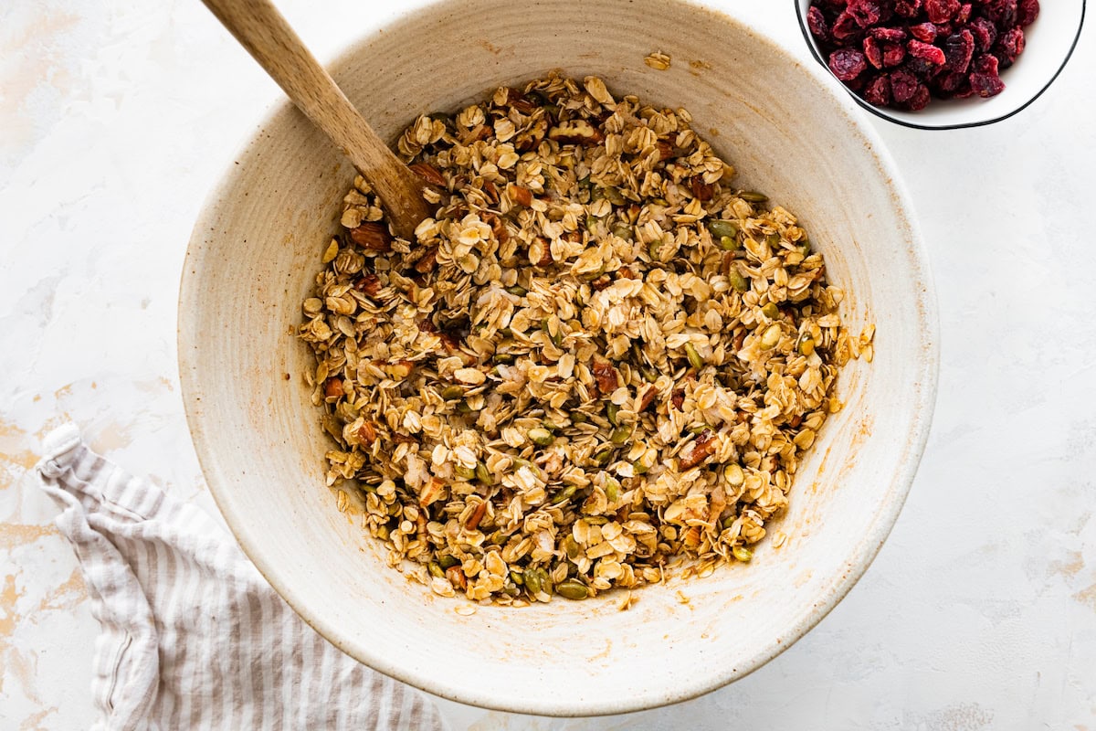 granola ingredients in mixing bowl with wooden spoon. 