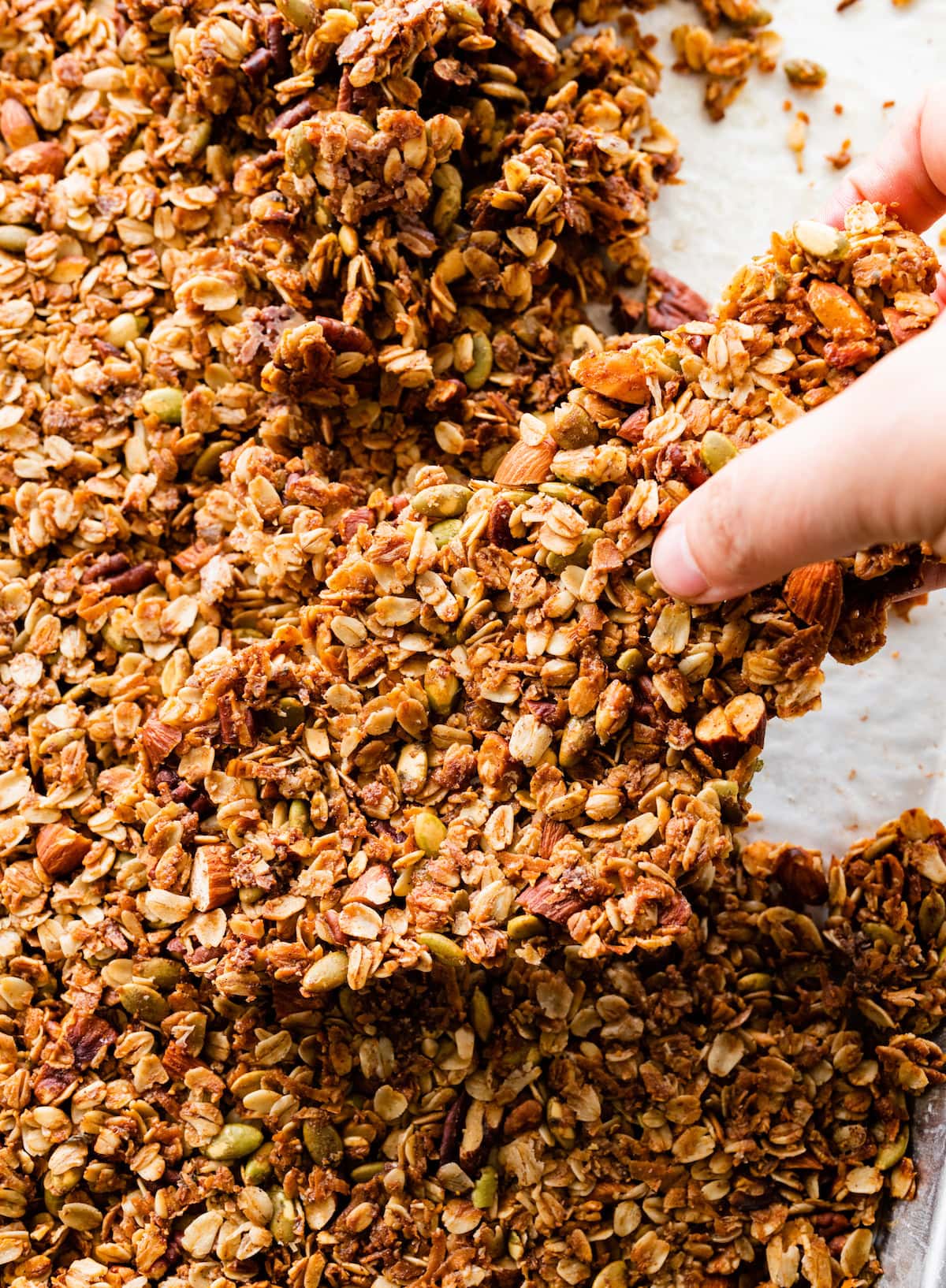 large granola cluster on baking sheet being broken up. 