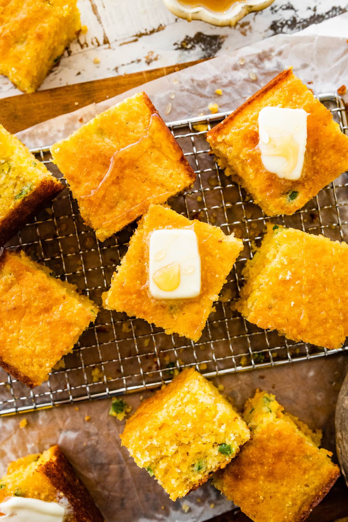 pieces of jalapeño cheddar cornbread on cooling rack with butter and honey. 