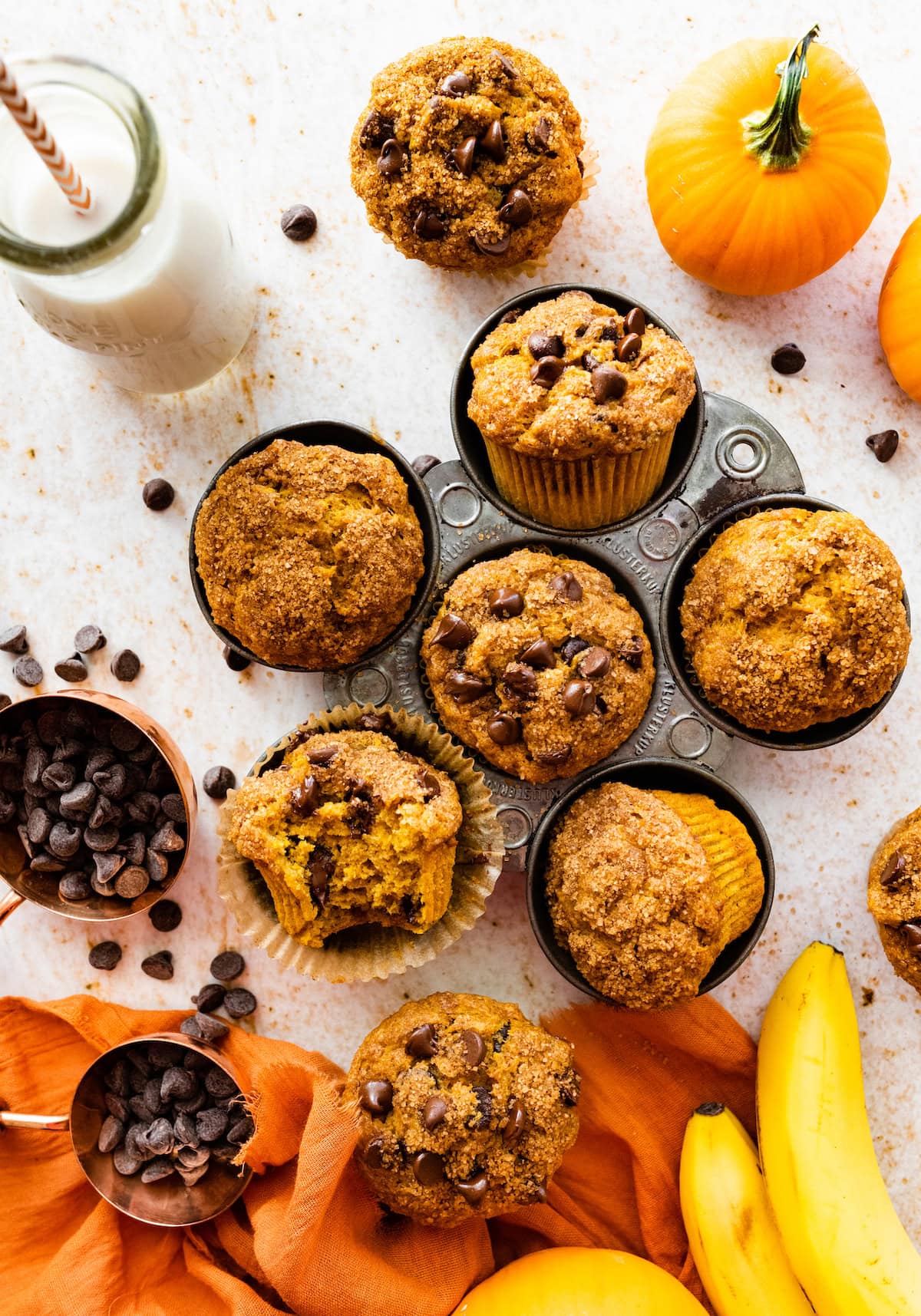 pumpkin banana muffins with chocolate chips in muffin tin and glass of milk. 