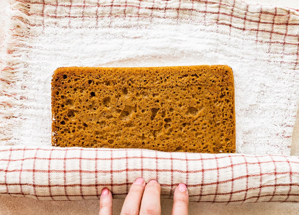 rolling up pumpkin roll cake in kitchen towel with confectioner's sugar. 