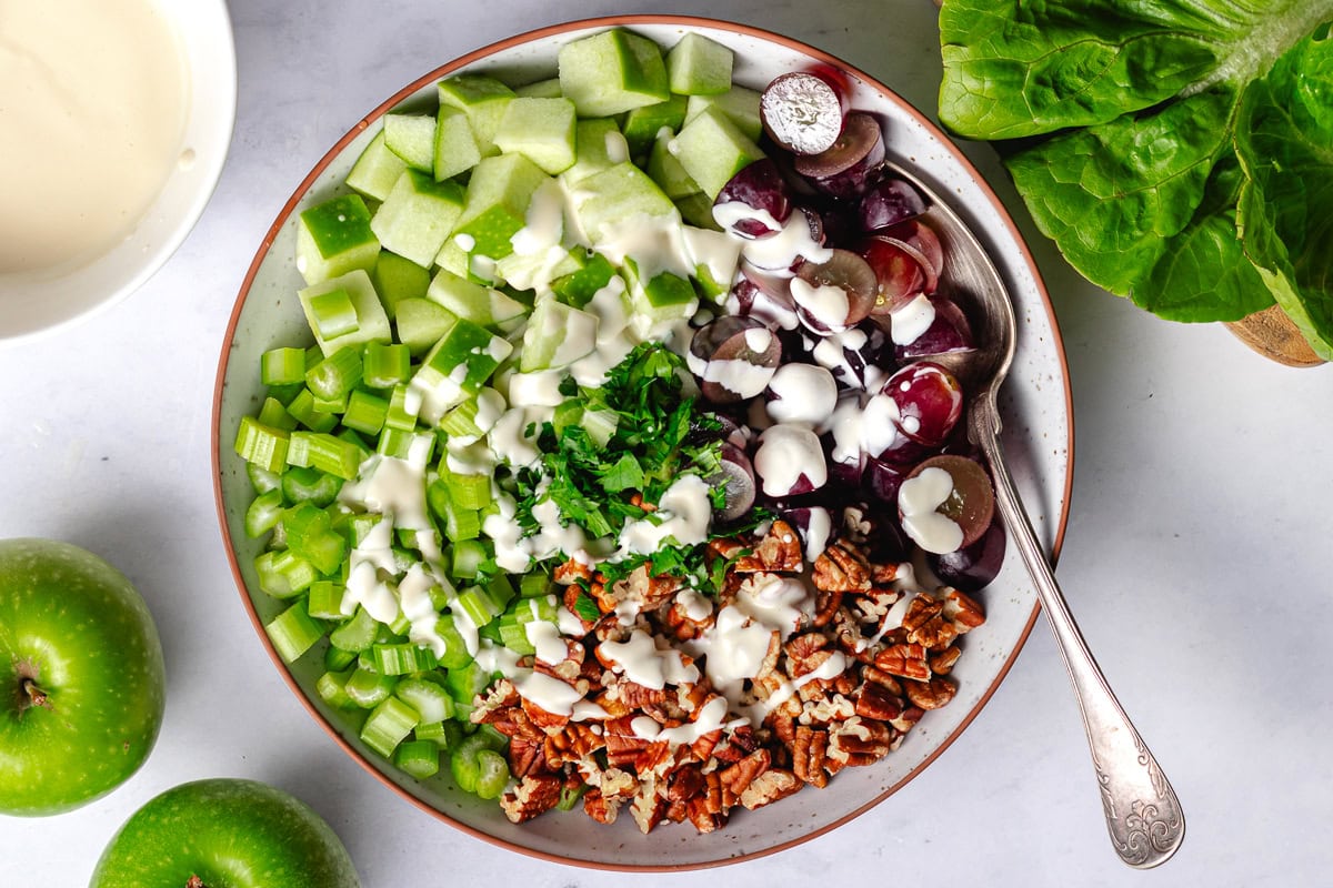 waldorf salad dressing being drizzled over the salad in bowl with spoon. 