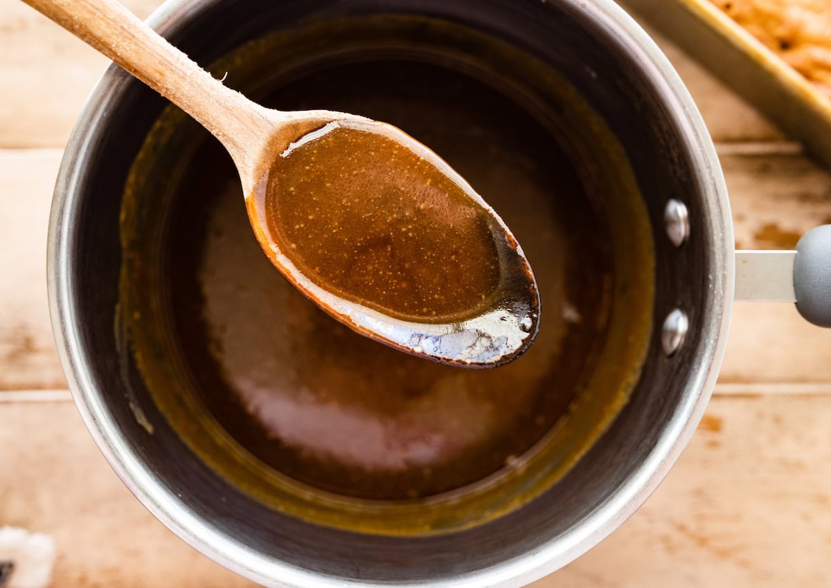 toffee sauce in spoon over saucepan of toffee sauce. 