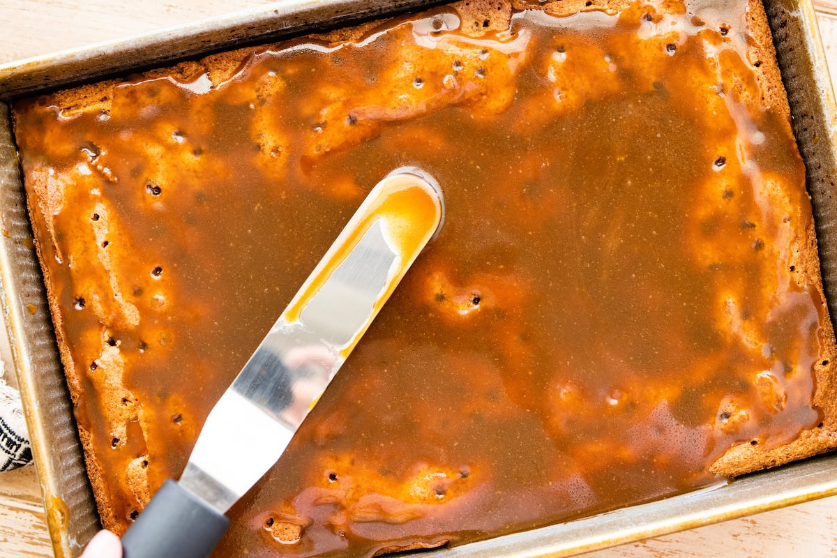 toffee sauce being spread over apple cake in pan. 