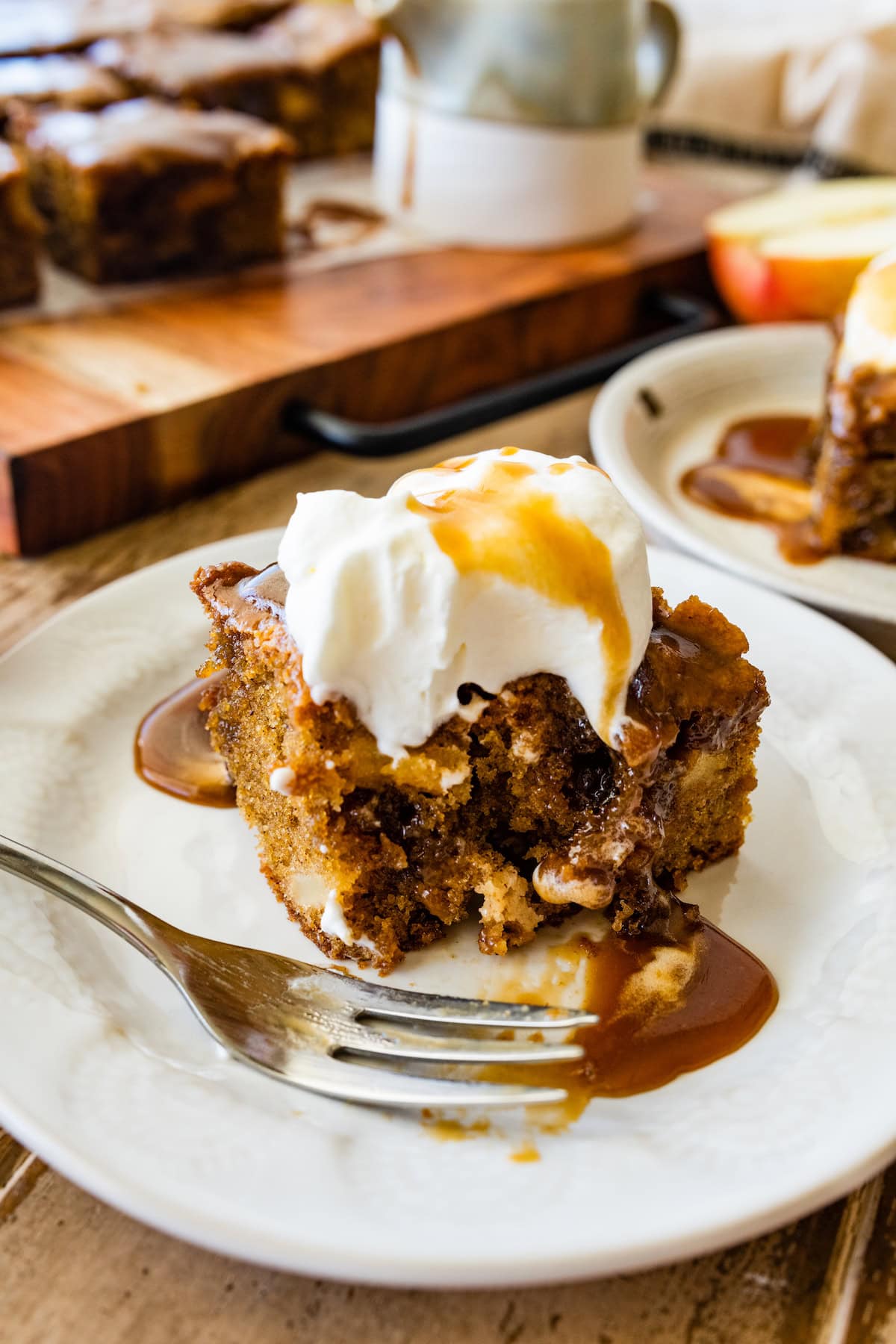 piece of apple cake with toffee sauce and whipped cream on plate with fork. 