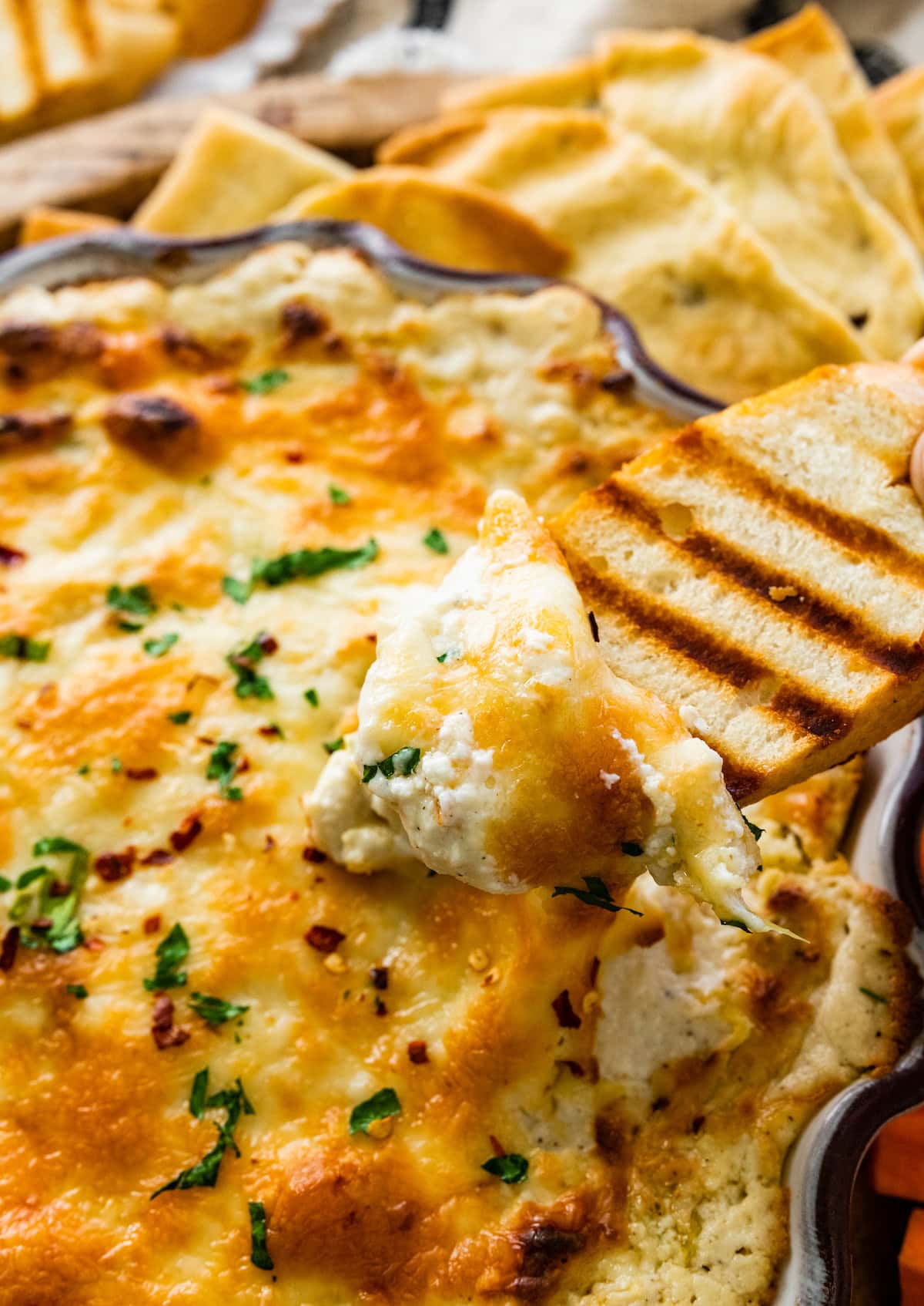 piece of grilled bread being dipped in artichoke dip. 