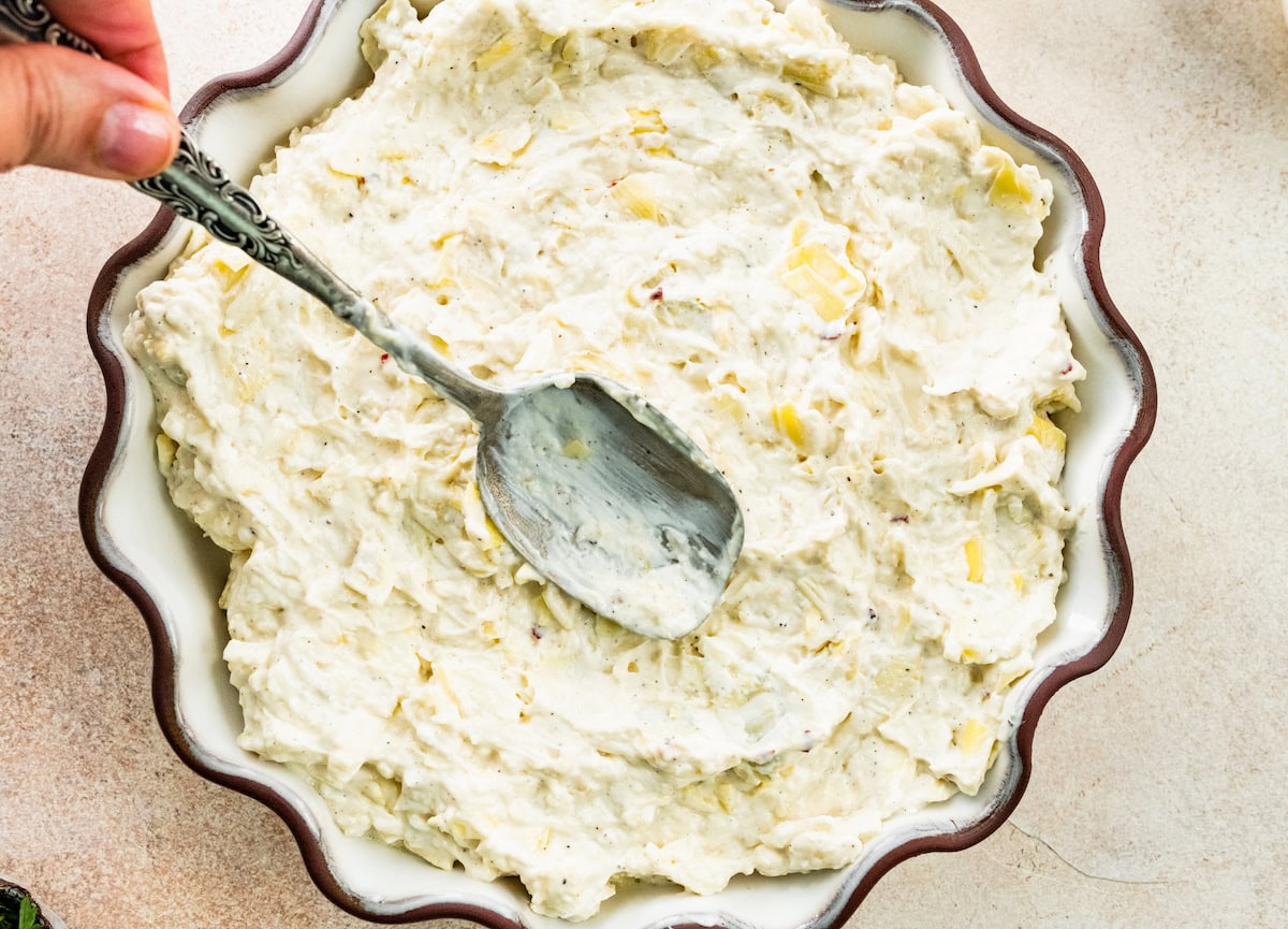 artichoke dip being spread in baking dish with spoon. 