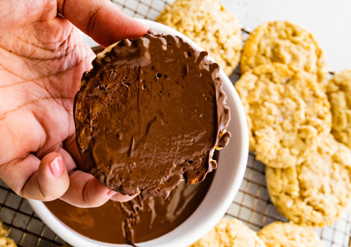 coconut cookies being dipped in melted chocolate. 