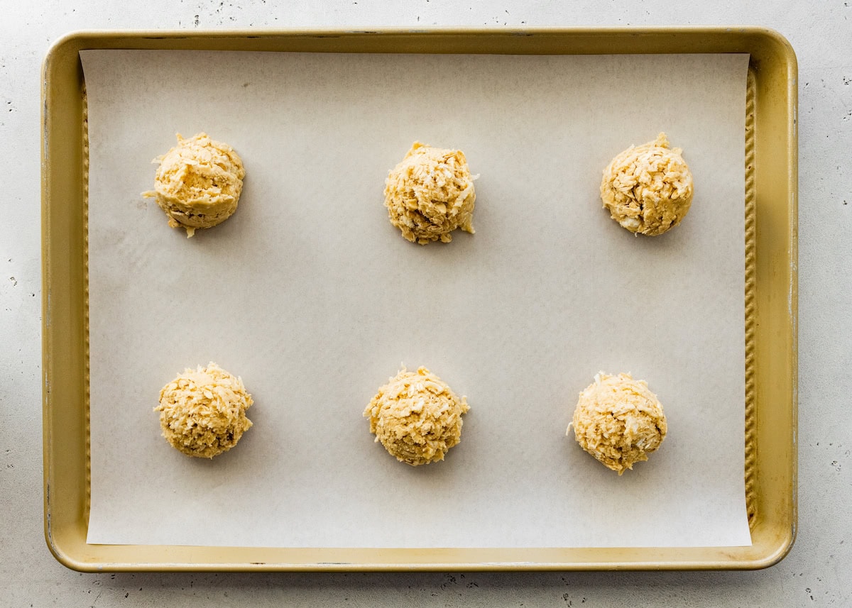 coconut cookie dough balls on baking sheet with parchment paper. 