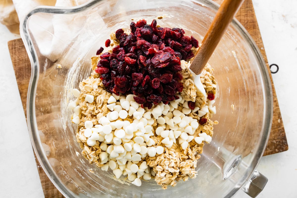 oatmeal cookie dough with white chocolate chips and dried cranberries in mixing bowl with spatula. 