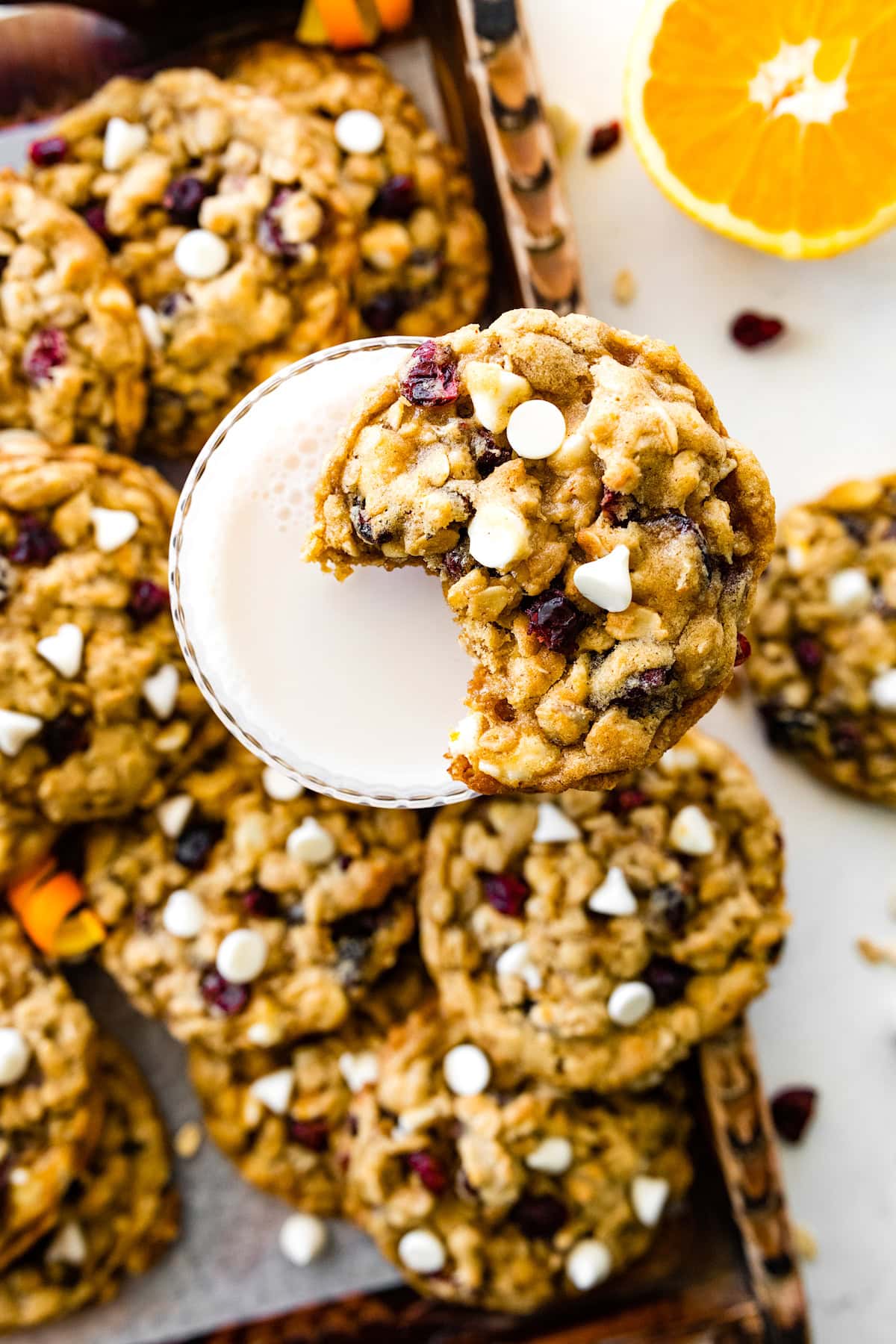 cranberry orange white chocolate oatmeal cookie with bite out of it on glass of milk. 