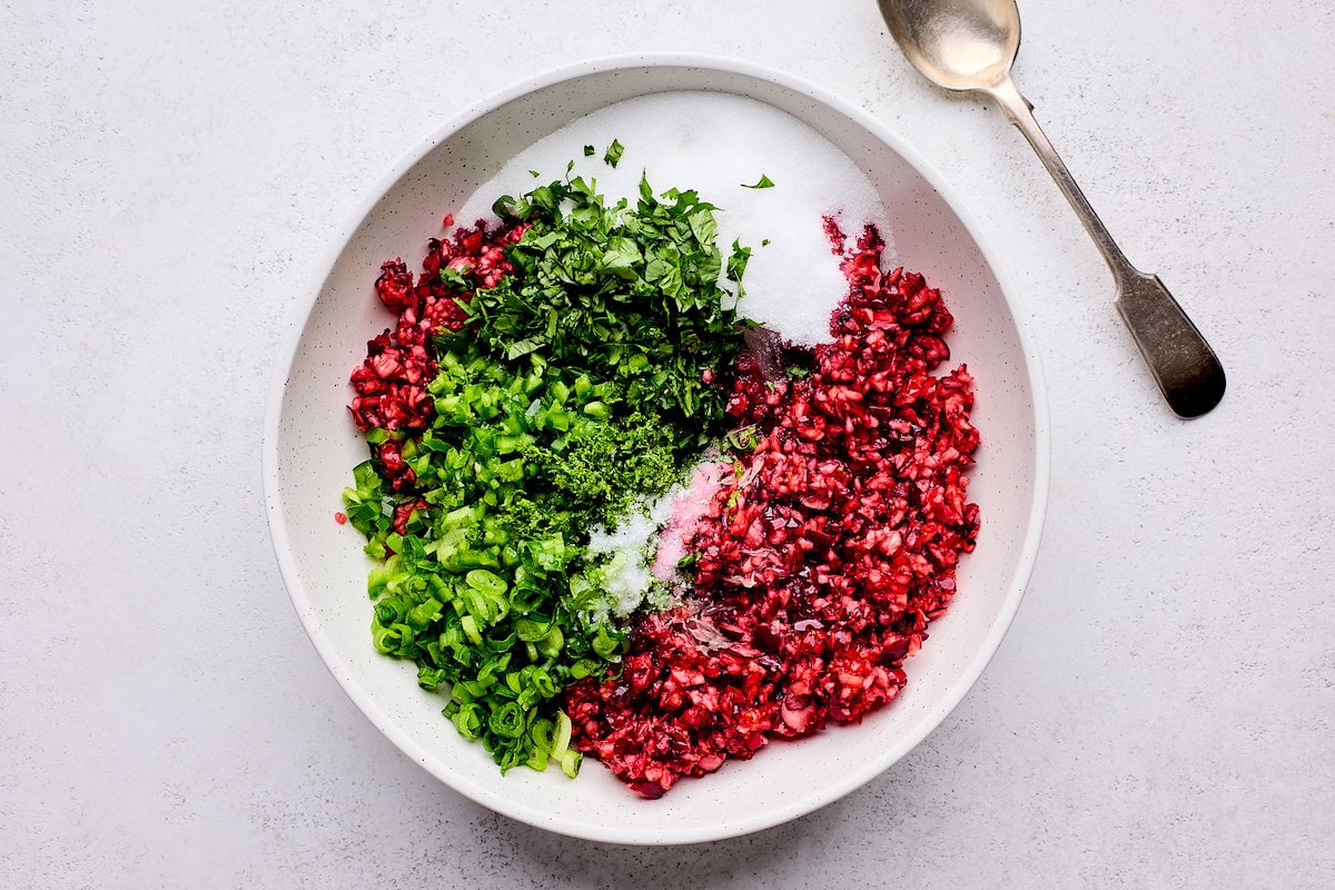 chopped up cranberries, cilantro, green onion, jalapeño, lime, and sugar in mixing bowl to make cranberry salsa. 