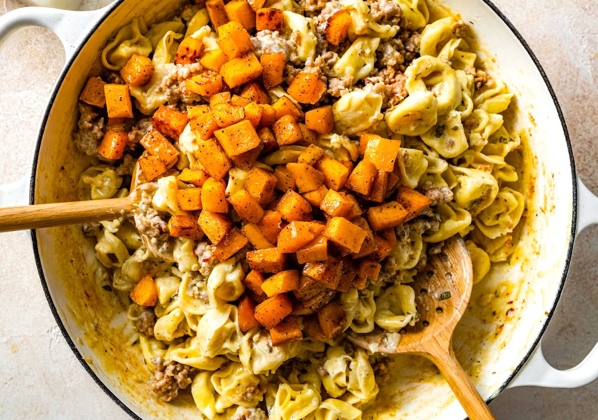 tortellini, sausage, and roasted butternut squash with cream sauce in pan with wooden spoons. 