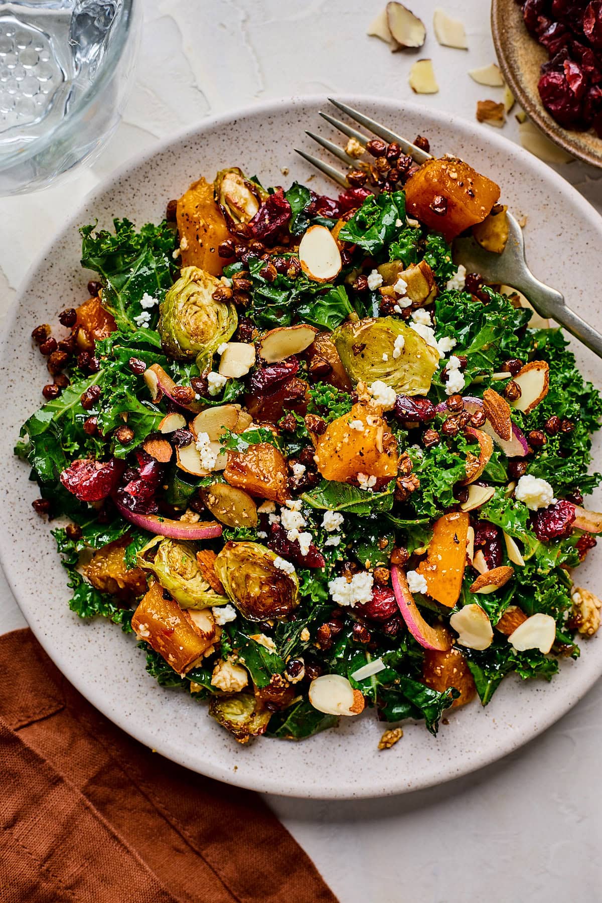 kale salad with roasted vegetables and crispy lentils on plate with fork. 