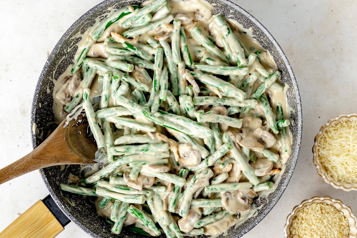 green beans and creamy mushroom sauce being stirred together in skillet with wooden spoon. 