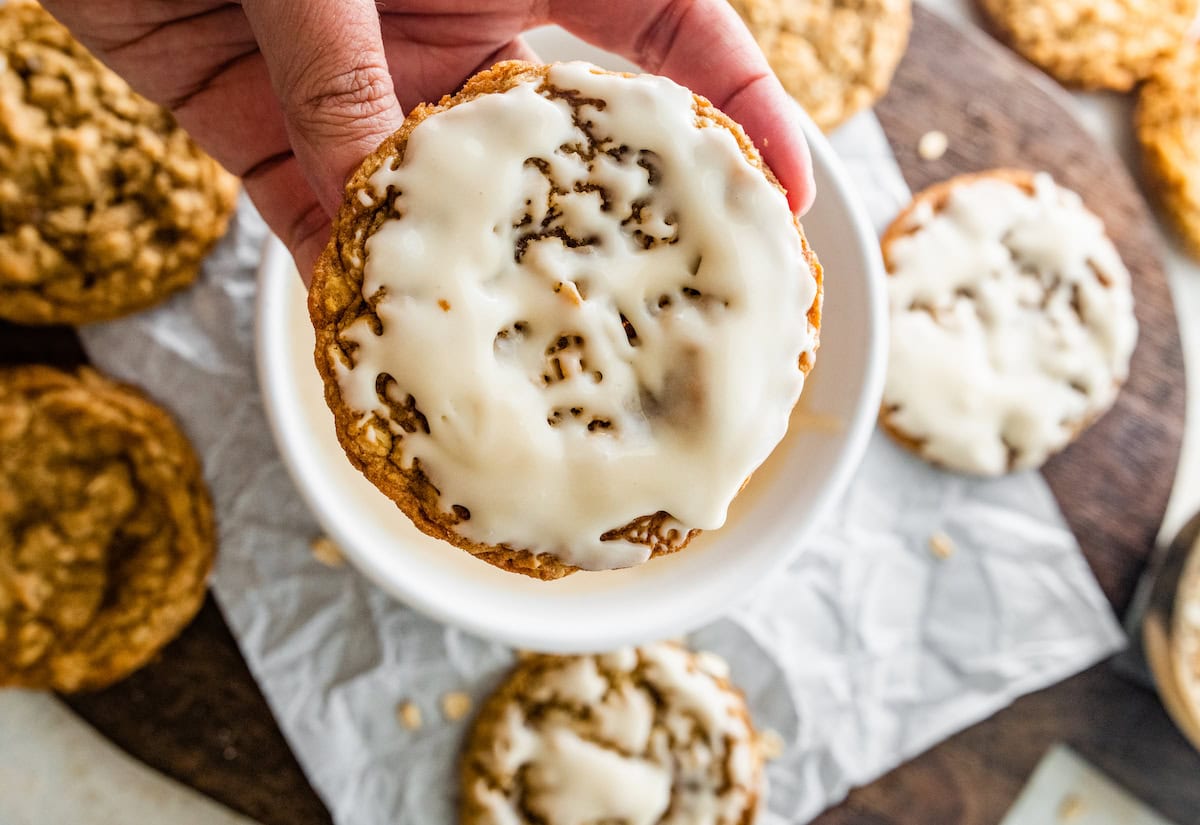 iced oatmeal cookies being dipped in icing. 