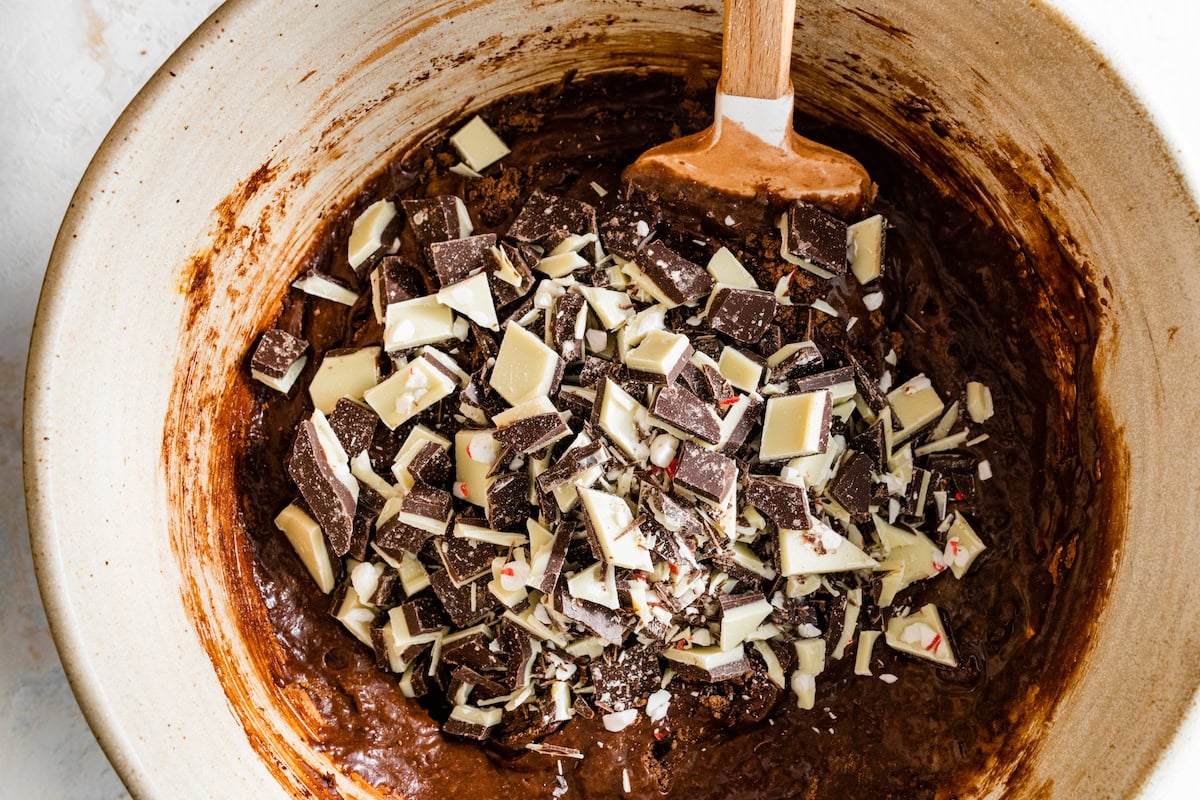 brownie batter in mixing bowl with chunks of peppermint bark. 