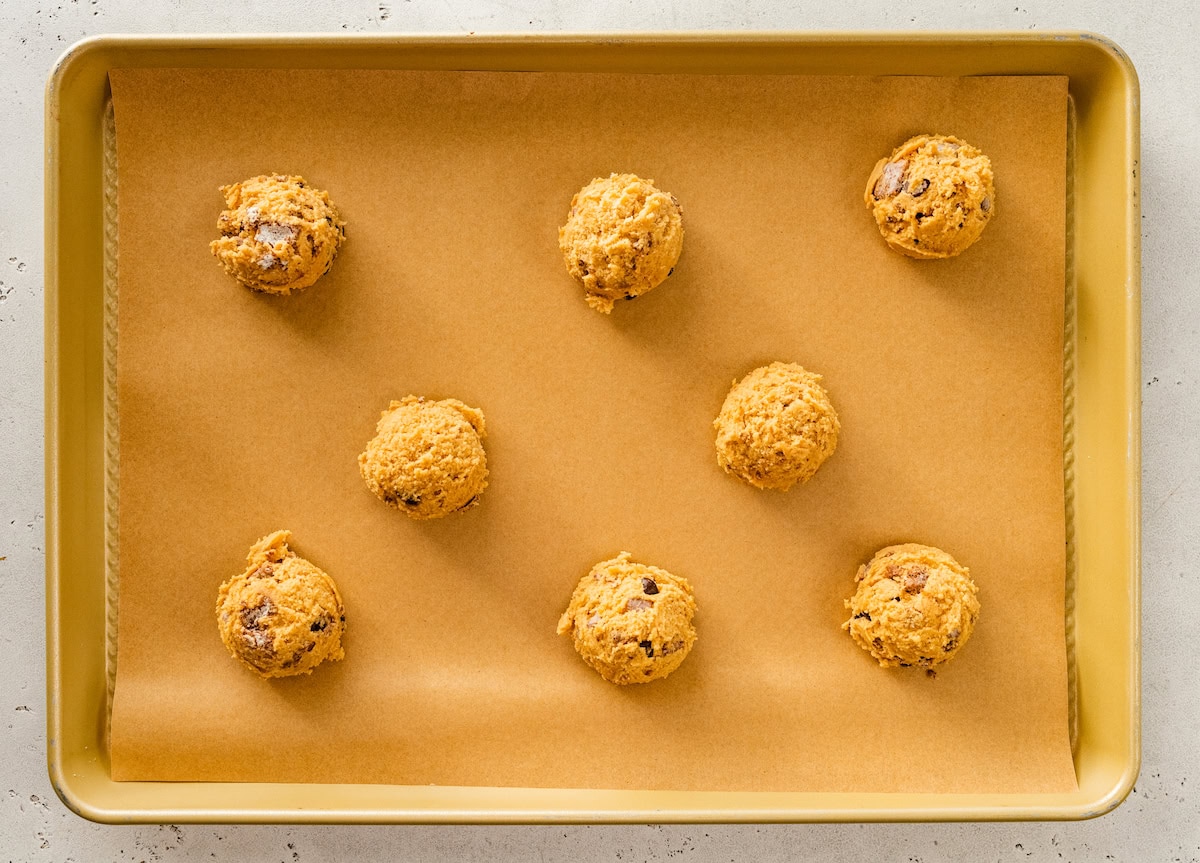 puppy chow cookie dough balls on baking sheet with parchment paper. 