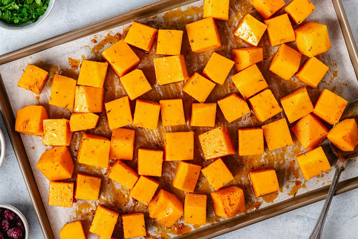 butternut squash cubes tossed in hot honey dressing on baking sheet with parchment paper. 