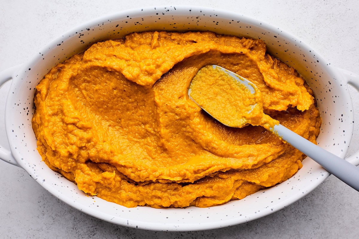 sweet potato casserole filling being spread in baking dish with spatula. 