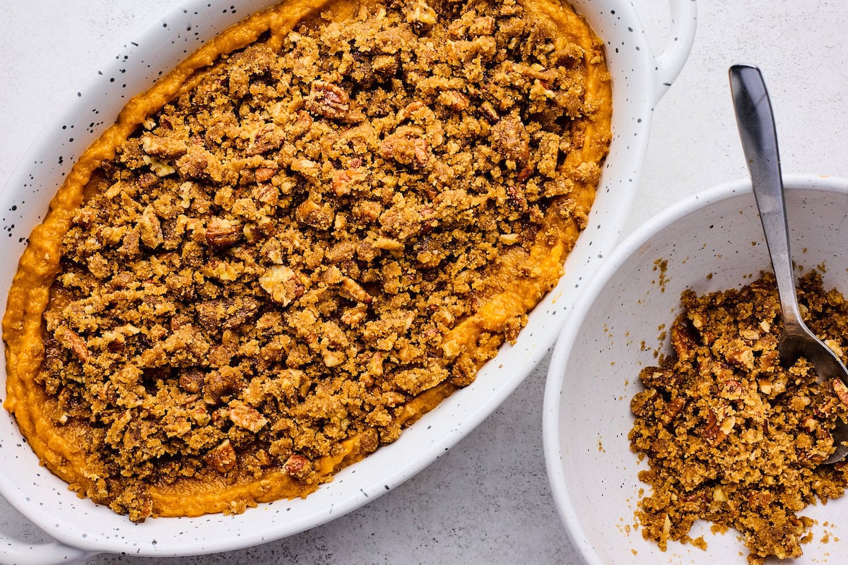 brown sugar pecan topping being sprinkled on top of sweet potato casserole in baking dish. 