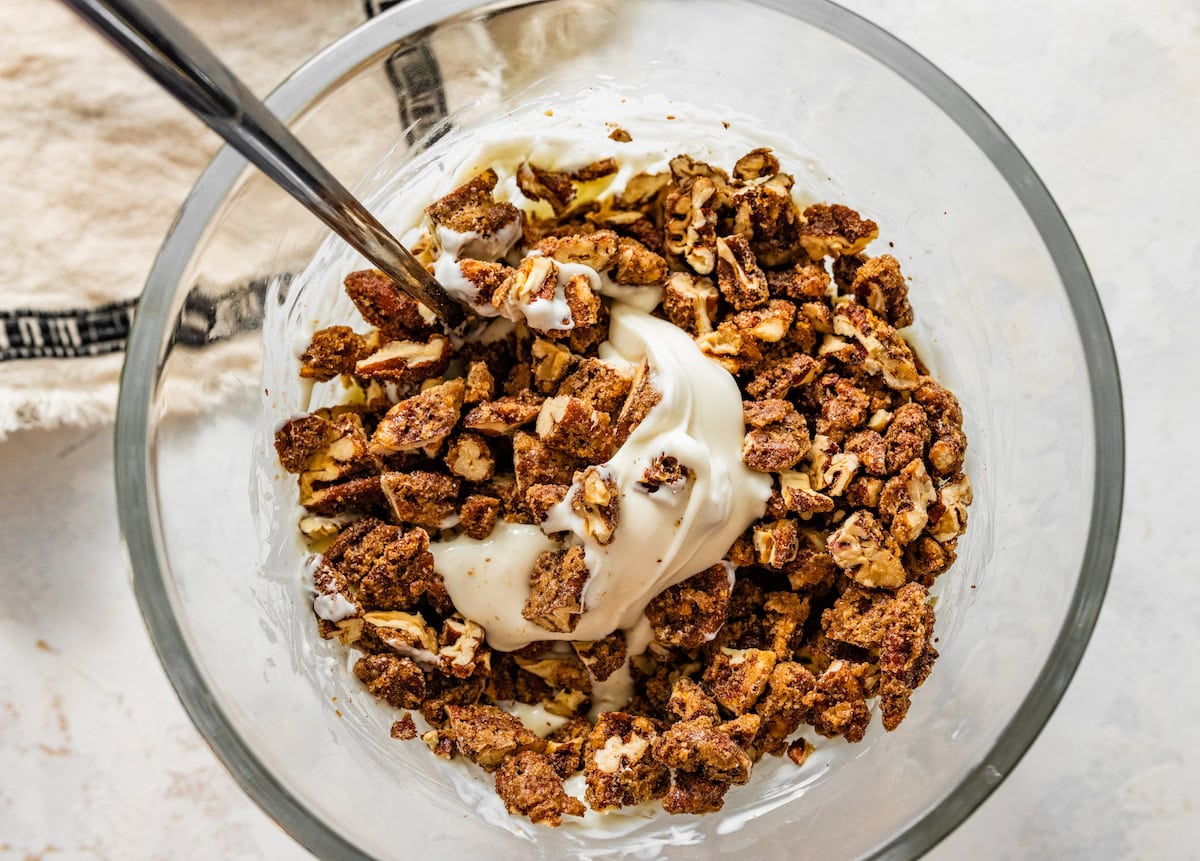 chopped candied pecans in bowl with melted white chocolate and spoon. 