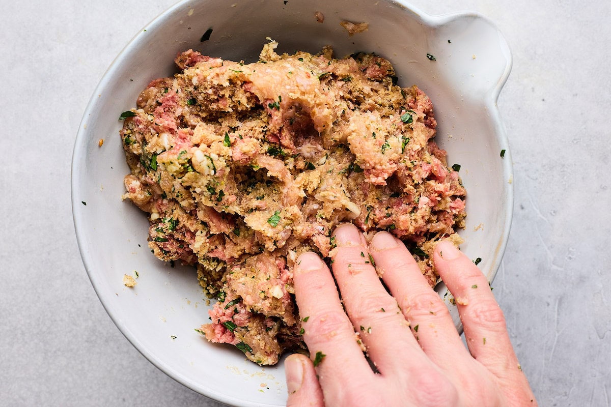 mixing meatball mixture in bowl with hand. 