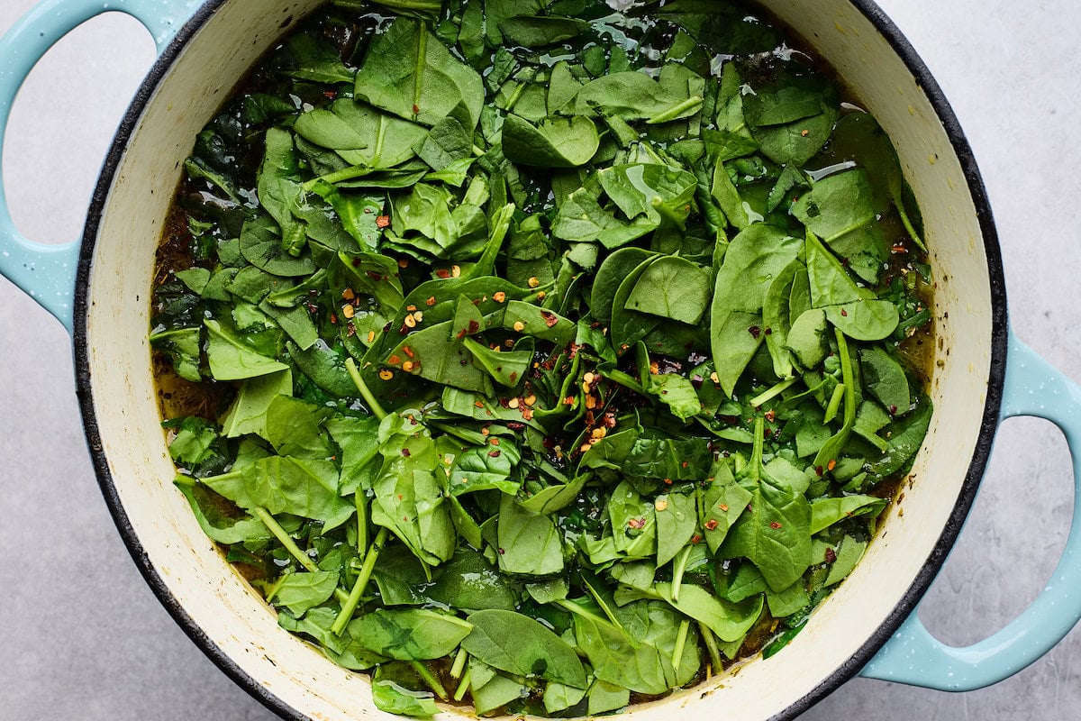 spinach and crushed red pepper flakes being added to pot of Italian wedding soup. 